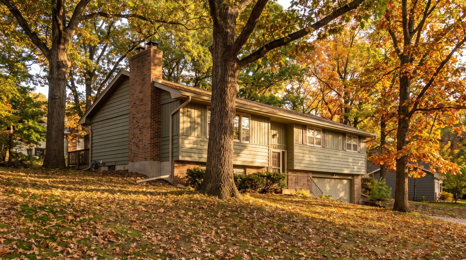 Post-war suburban house with a brick-veneer chimney against a wooded hillside