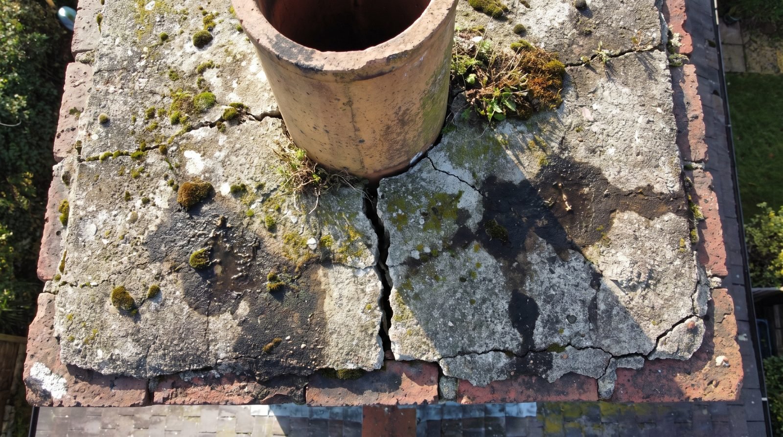Cracked concrete chimney crown with a hairline fracture running from the flue tile to the edge