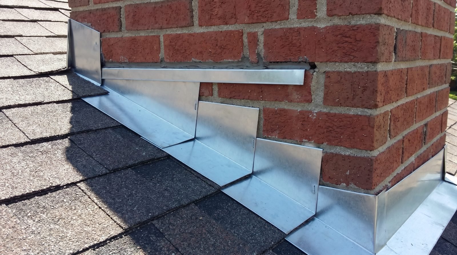 Step and counter flashing at the joint between a brick chimney and an asphalt shingle roof